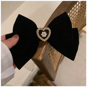 Detailed close-up of large black velvet bow hair claw with camellia and rhinestone heart