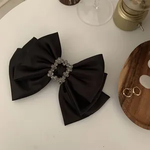 Detail of elegant black satin bow hair clip with a sparkling square rhinestone centerpiece