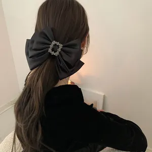 Detailed back view of a black satin bow hair clip with a square rhinestone center on long hair
