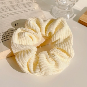 Detail eines cremefarbenen Cord-Haargummis mit Rippstruktur auf einem offenen Buch