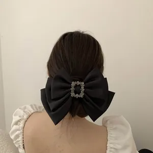 Detailed view of a black satin bow hair clip with a sparkling square rhinestone buckle
