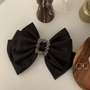 Elegant large black satin bow hair clip with a square diamond buckle on a white surface