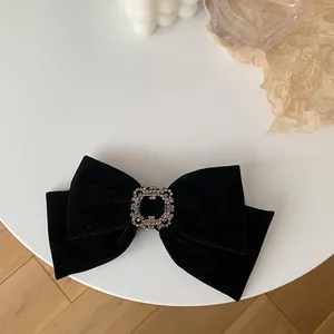 Detail of a black velvet bow hair clip with a square diamond center on a white table