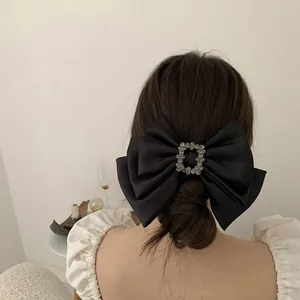 Detail of a large black satin bow hair clip with a square rhinestone center on a model