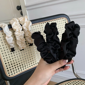 Detailed view of wide pleated satin headbands in black and cream on a rattan chair