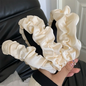 Macro shot of cream-colored pleated satin headband with elegant silk texture and wide band