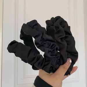 Close-up of three black pleated headbands with elegant satin texture and shiny finish