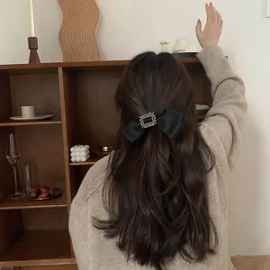 Détail d'une grande pince à cheveux nœud en satin noir avec boucle carrée en strass