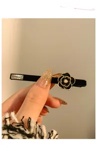 Dettaglio fermaglio camelia nera vintage con perla bianca e targhetta in metallo LOVEDAYS