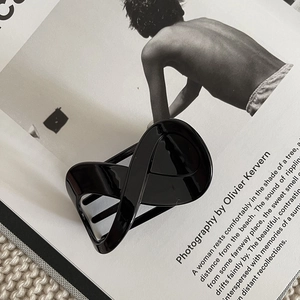 Detail of glossy black infinity hair claw clip on minimalist magazine background