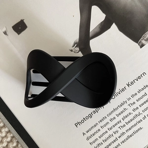 Detail view of the matte black figure-eight hair claw clip with a sleek crossed design