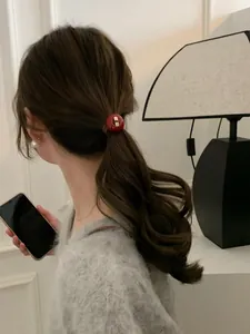 Detailansicht eines vintage roten Acrylknopf-Haargummis auf gewelltem braunem Haar