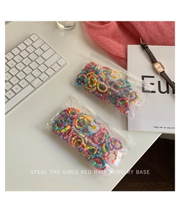 Close-up of assorted colorful elastic hair ties in a daisy print zipper pouch on white desk