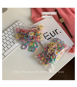 Colorful elastic hair bands set in a clear daisy pouch next to a laptop and sweater