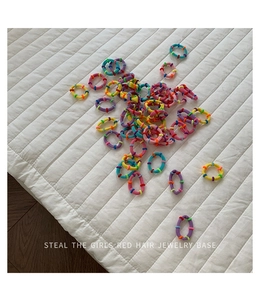 Close-up of assorted colorful elastic hair ties with beads on a soft white quilted surface