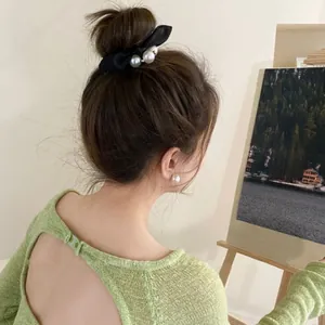 Detail view of elegant black bow hair tie and large pearl earrings worn by a model
