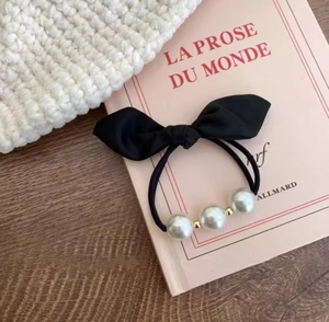 Close-up of a French vintage black bow hair tie with elegant pearls and gold beads on a book