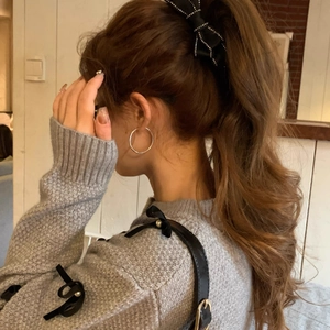 Detail view of large black bow banana clip and silver hoop earring on a model