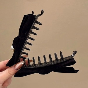 Détail d'une pince à cheveux en velours noir avec perle blanche et clip banane vertical