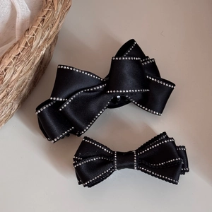 Detail of black satin bow hair clip with sparkling rhinestone edges and metal spring mechanism