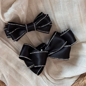 Elegant black satin bow hair clips with rhinestone edges on soft textured fabric background