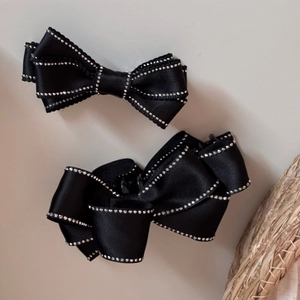 Detail of two black satin bow hair clips featuring sparkling rhinestone edges and metal base