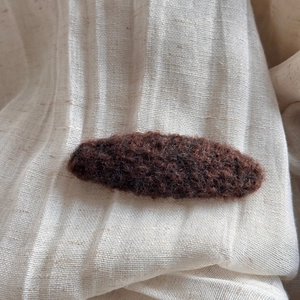 Close-up of deep brown fuzzy plush hair clip with thick curled fiber texture on beige fabric