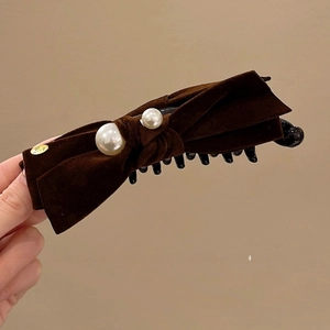 Détail d'une barrette à nœud en velours marron ornée de perles blanches et d'un médaillon Love