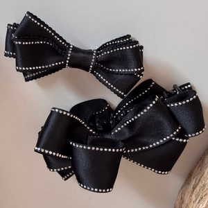 Elegant black satin bow hair clip set with silver rhinestones on beige background