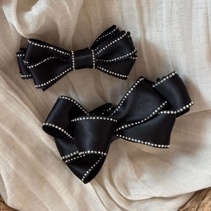 Detail of black satin bow hair clips with sparkling rhinestone edges on beige fabric