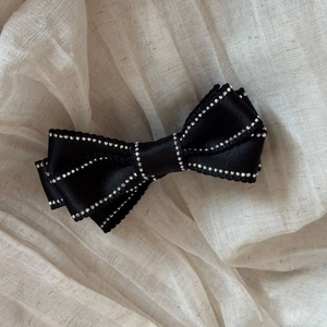 Detailed close-up of a black satin bow hair clip with fine silver bead edge detailing