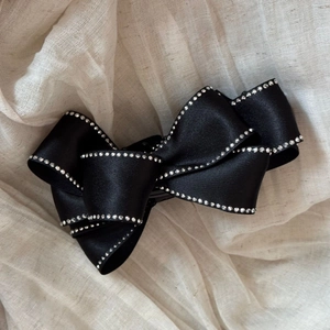 Detail showing elegant black satin bow hair clip with sparkling rhinestone edge accents