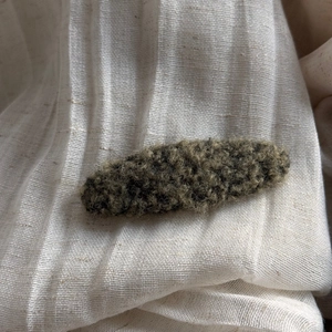 Detail of plush lamb wool hair clip in dark brown and olive green on linen fabric