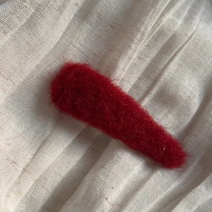 Close-up of deep red plush velvet hair clip texture on minimalist beige fabric background