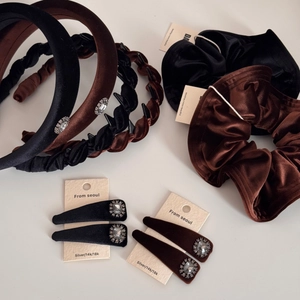 Flat lay of velvet braided headband, scrunchie and rhinestone hair clip in black and brown