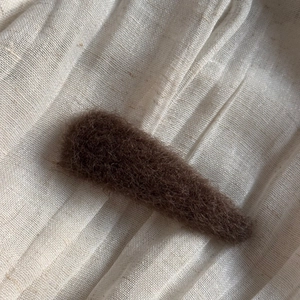 Detailed close-up of dark brown plush hair clip on soft beige textured fabric