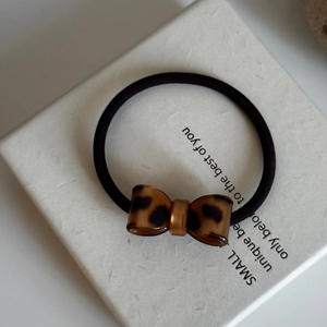 Detailed view of elastic hair tie with leopard print resin bow on neutral background