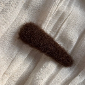 Detail of a dark brown plush oval hair clip on a natural white linen fabric surface