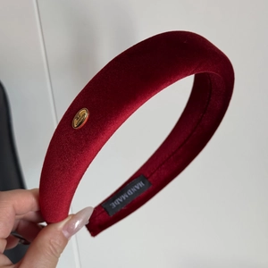 Detail shot of a red velvet padded headband featuring a golden handmade metal label tag