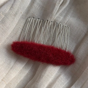Close-up of fluffy red oval hair comb with silver metal teeth on soft linen fabric