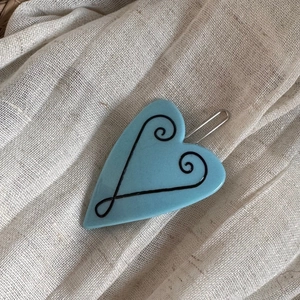 Detail einer himmelblauen herzförmigen Haarspange mit schwarzen Wirbelmustern