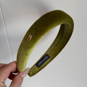 Detail of olive green velvet headband featuring a handmade gold metal tag and thick padding
