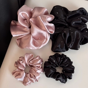 Detail of four satin hair scrunchies in pink and black with sparkling rhinestone accents