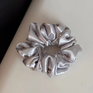Detail of silver grey satin scrunchie with rhinestones on a textured background