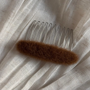 Close-up of deep brown plush oval hair comb with ten silver metal teeth on linen fabric