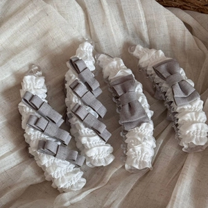 Detail van vier bananenklemmen met witte kant en grijze linnen strikken op een linnen textuur