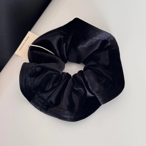 Detail shot of a black velvet scrunchie showing soft pleated texture and premium fabric gloss