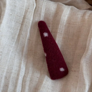 Détail de la pince à cheveux en feutre rouge à pois blancs sur tissu beige