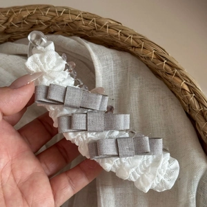 Detailopname van witte kanten haarklem met drie grijze strikken vastgehouden in hand