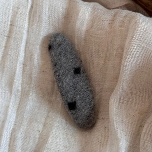 Texture détaillée de la barrette en feutre de laine gris foncé avec des pois noirs sur lin